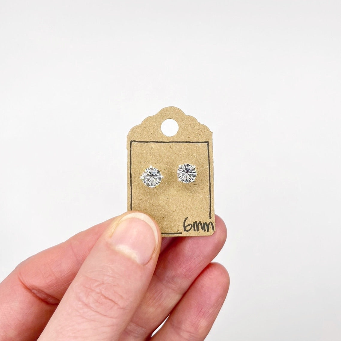 Silver stud earrings with clear cut glass on a cardboard tag held by a hand against a white background