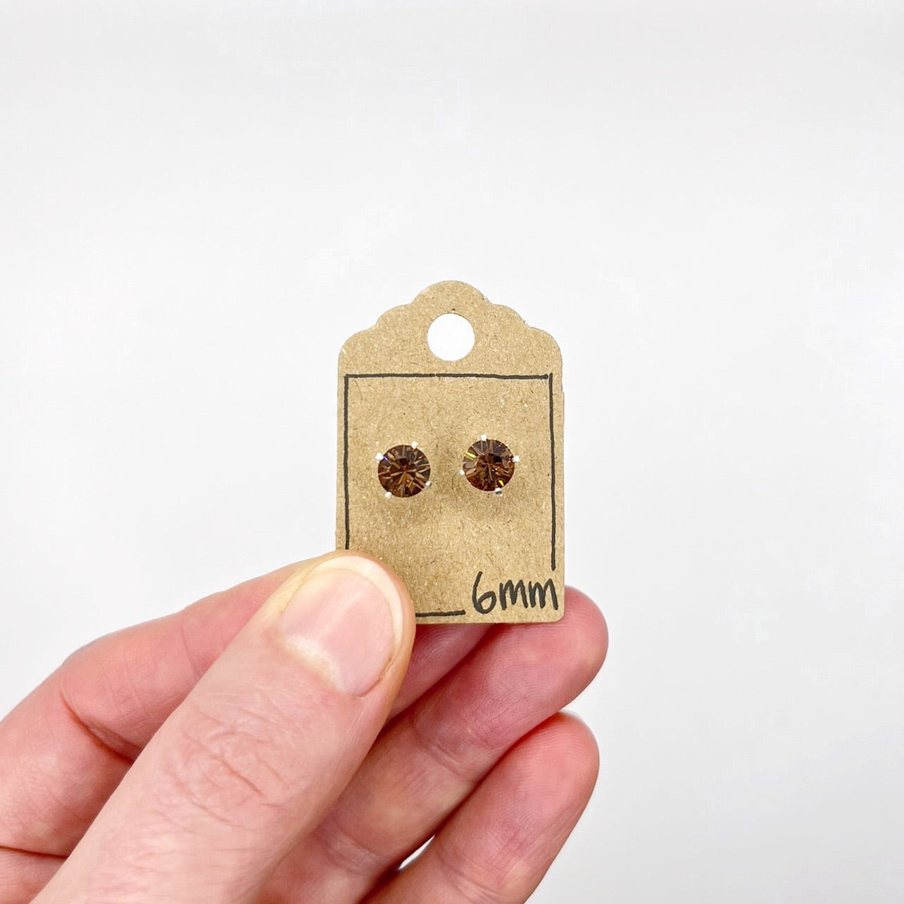 Small brown earring card with cut glass stud earrings held by a hand on a white background