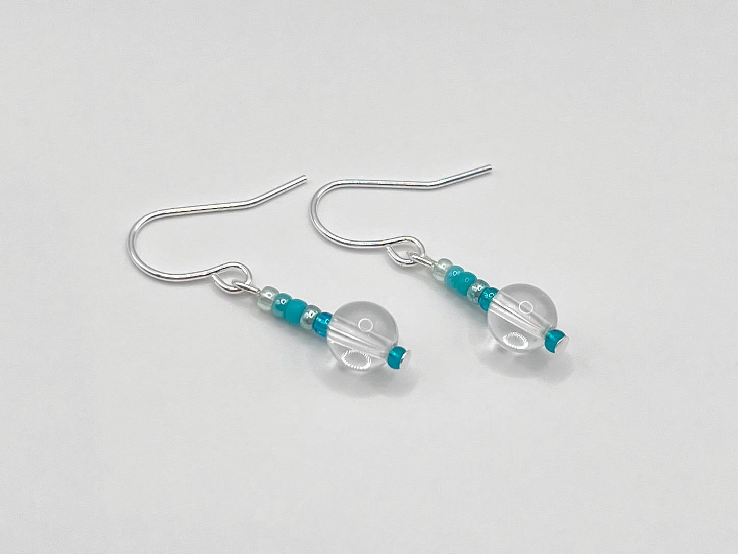 Pair of silver earrings with clear crystal and turquoise seed beads laid on a white background
