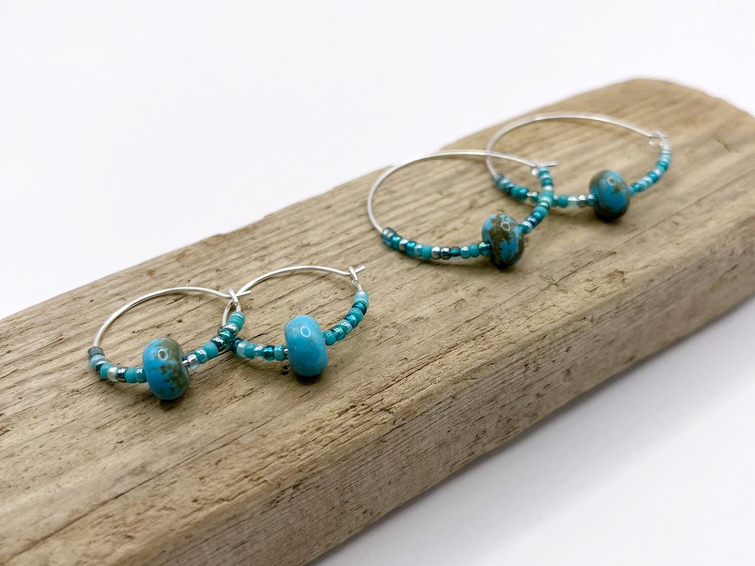 Two pairs of turquoise beaded hoop earrings laid on driftwood