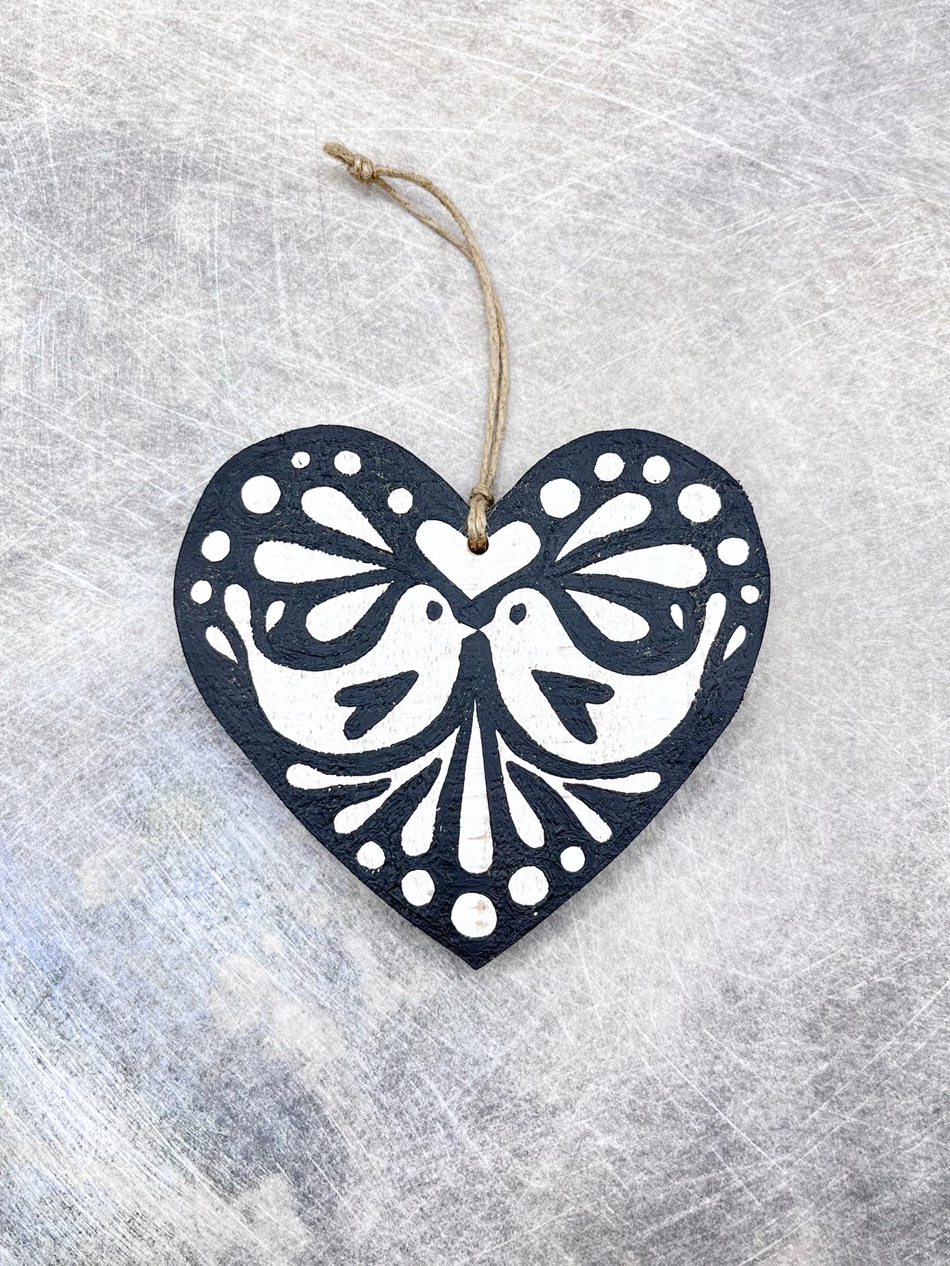 Black heart-shaped wooden hanging decoration with folk style love bird print   laid on a textured surface.