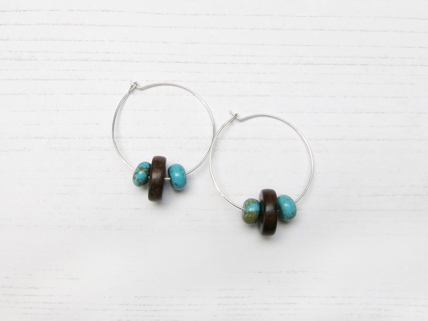 Pair of silver hoop earrings with wooden and turquoise beads on a white background