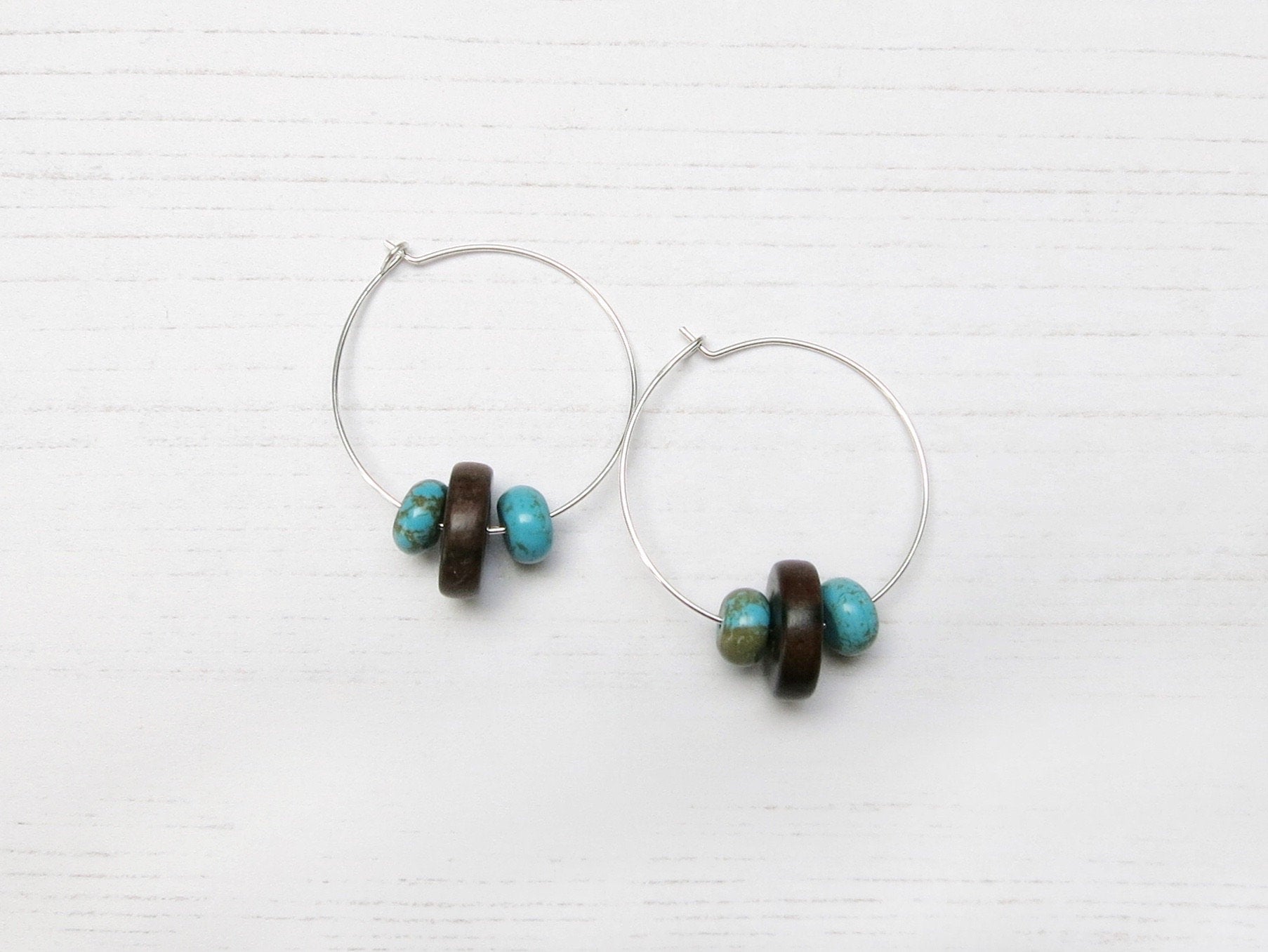 Pair of silver hoop earrings with wooden and turquoise beads on a white background