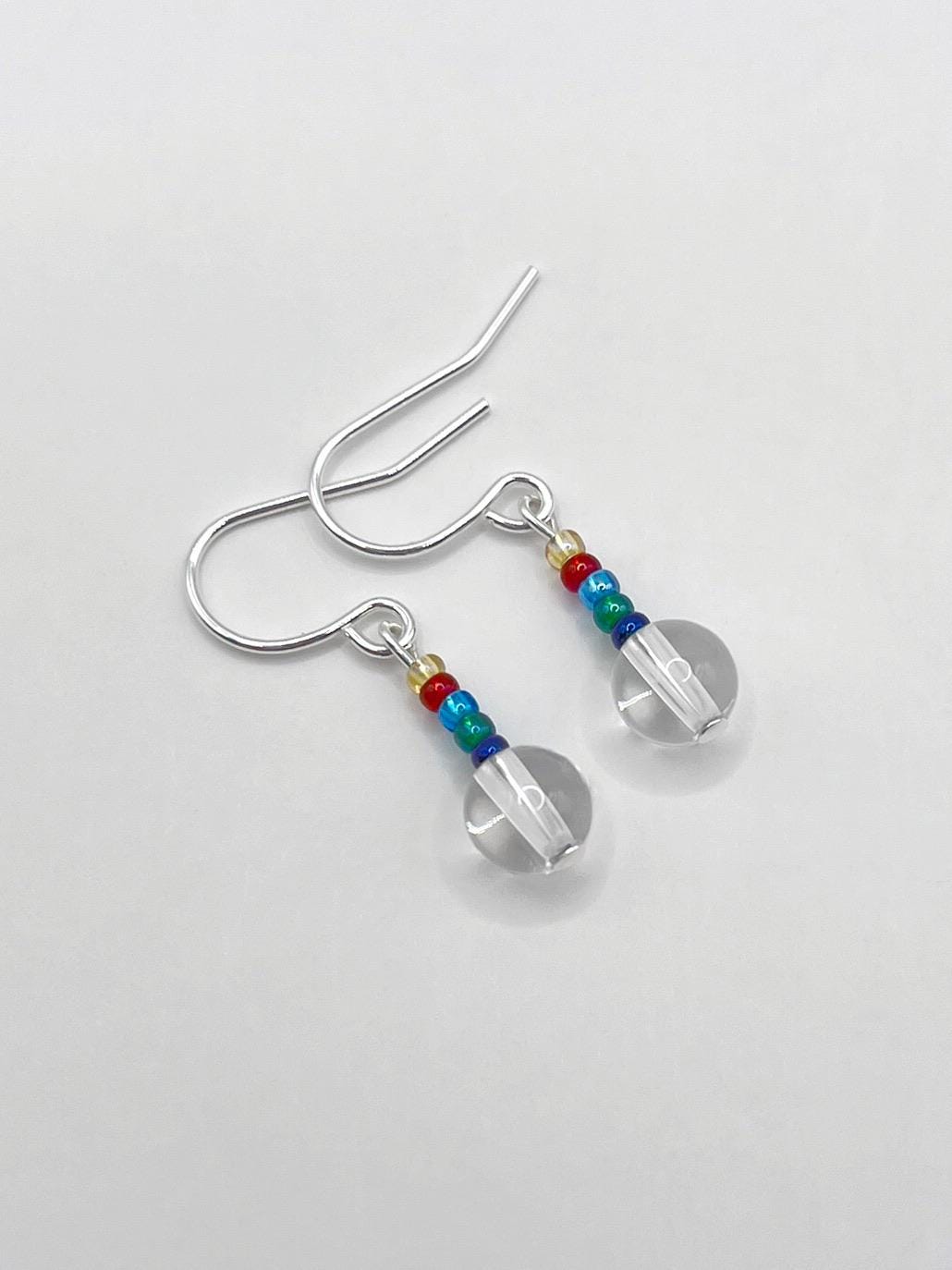 Pair of silver earrings with clear crystal rainbow seed beads laid on a white background