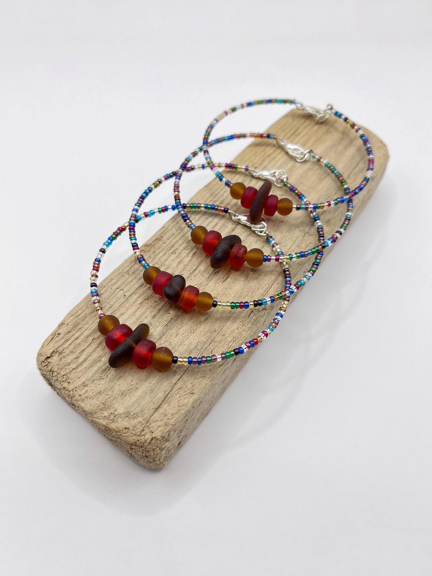 Rainbow beaded bracelets with sea glass and frosted glass beads laid on a wooden block with a white background