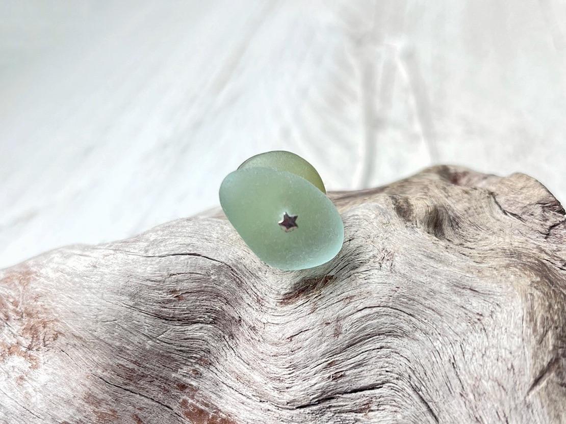 Close up showing the tiny silver star detail at the base of the sea glass pendant, laid on driftwood
