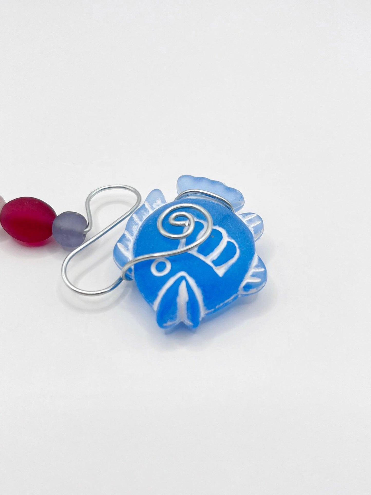 Close up of decorative hanging mobile with blue fish, wire and colourful beads on a white background