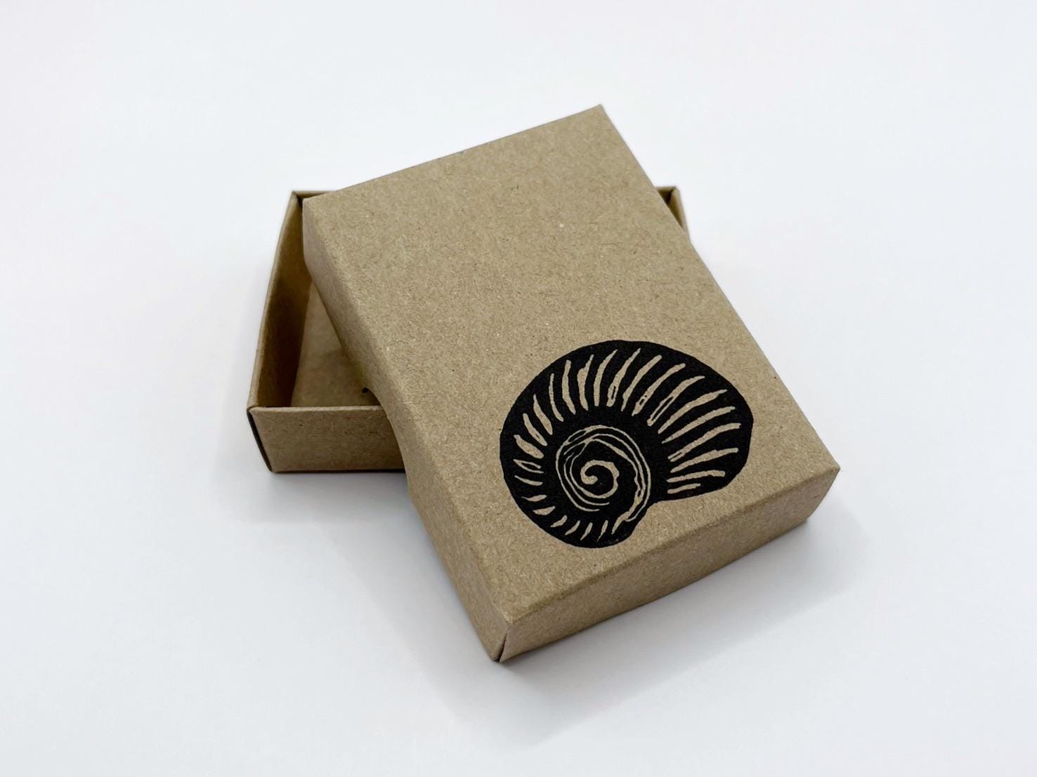 Brown cardboard box with a hand printed black shell design on a white background