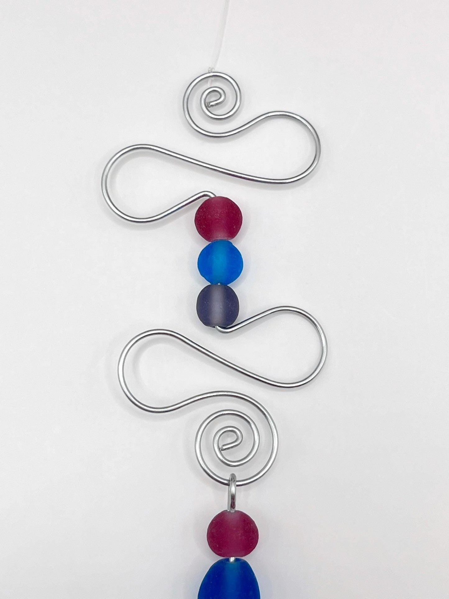 Close up of decorative hanging ornament with blue fish design, wire and colourful beads, laid  on a white background