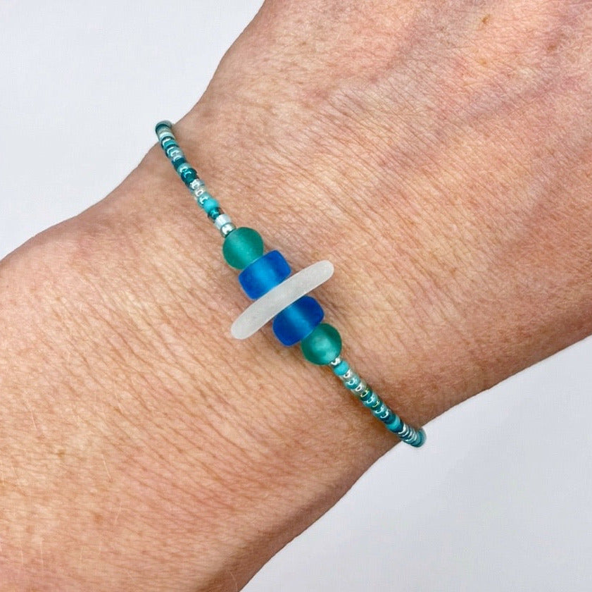 Close up of bracelet with white sea glass and blue and turquoise beads worn on a wrist against a white background