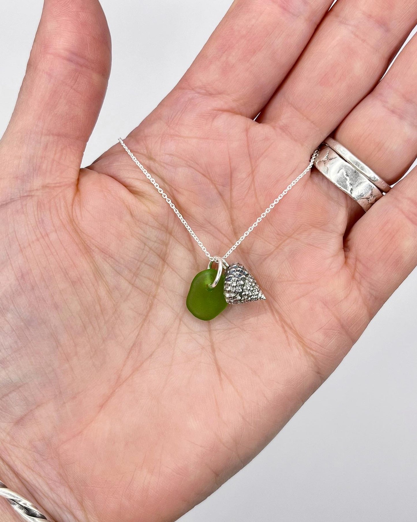 Necklace with green sea glass and silver shell pendant held in a hand against a white background