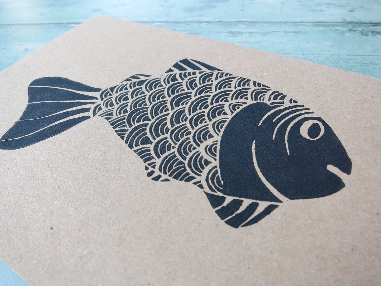 close up of Kraft paper card with original lino printed fish laid on a textured surface. 