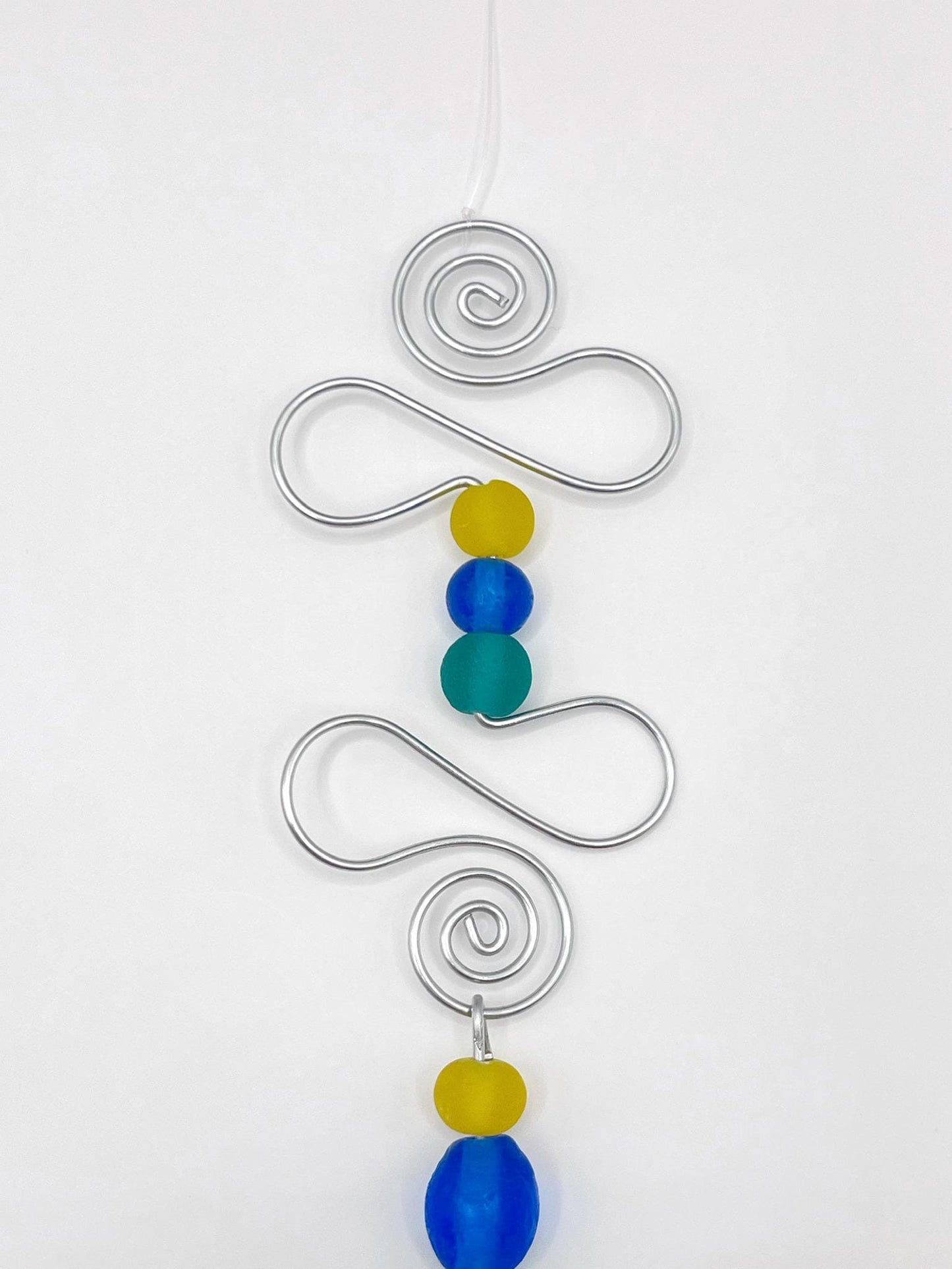 Close up of decorative ornament with blue fish design, wire and colourful beads on a white background