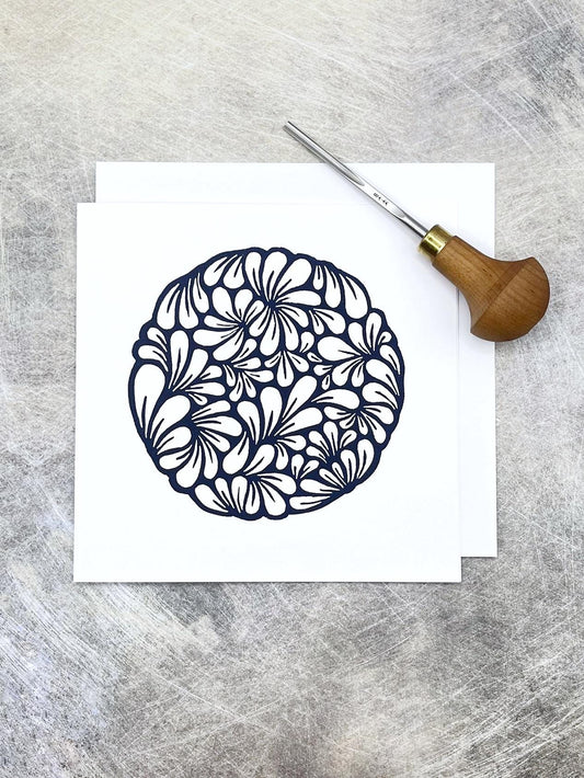 Original navy blue lino printed mussel shell pattern on white card laid on a textured background. Photo includes lino cutting tool.