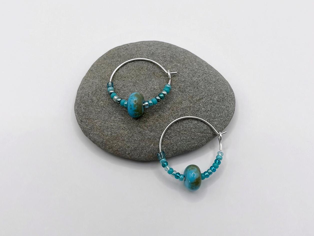Pair of hoop earrings with turquoise beads laid on a grey pebble