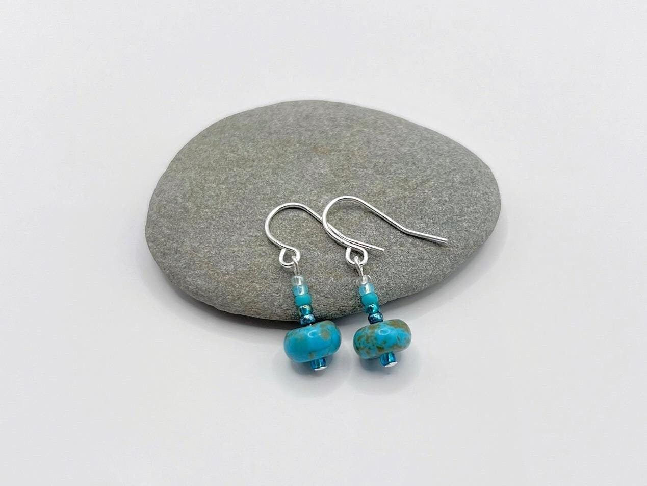 Pair of turquoise beaded earrings on a grey pebble with a white background