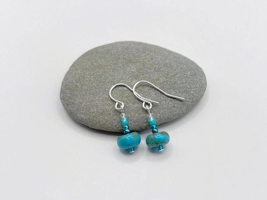 Pair of turquoise beaded earrings on a grey pebble with a white background