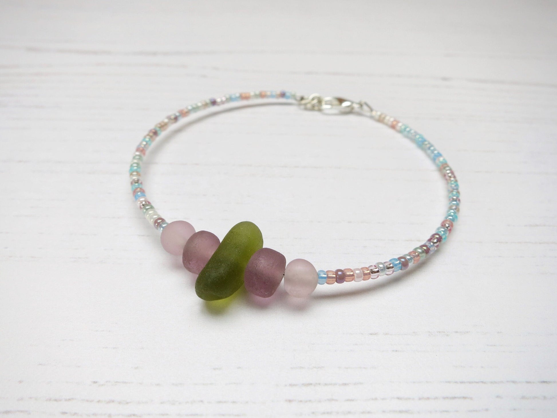 Pastel seed beaded bracelet with olive green sea glass laid on a pale background