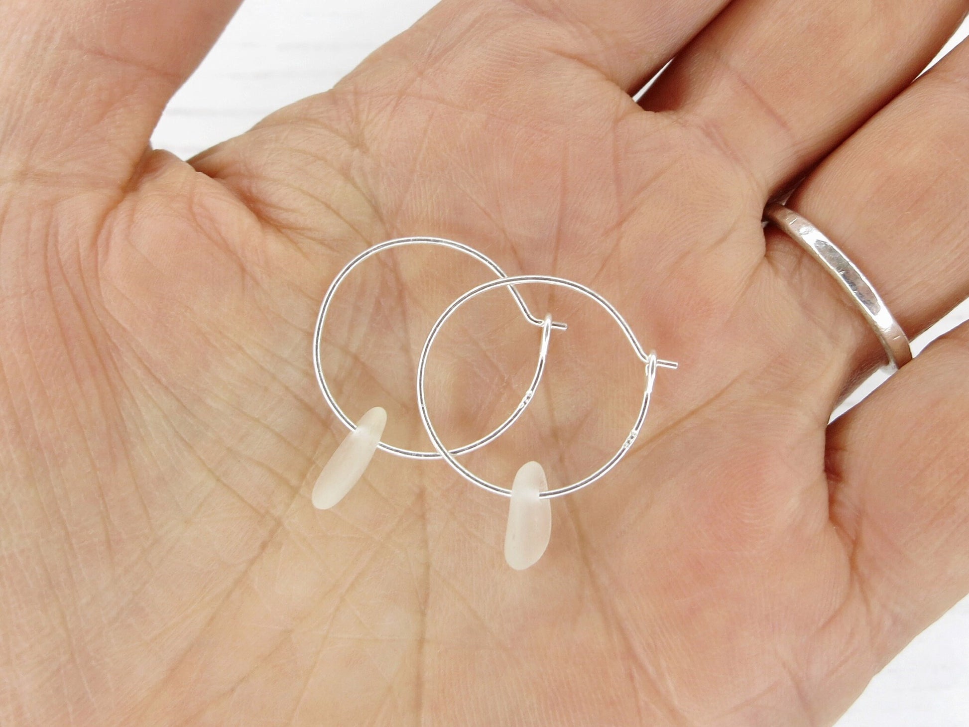 Silver hoop earrings with sea glass held in a hand against a white background