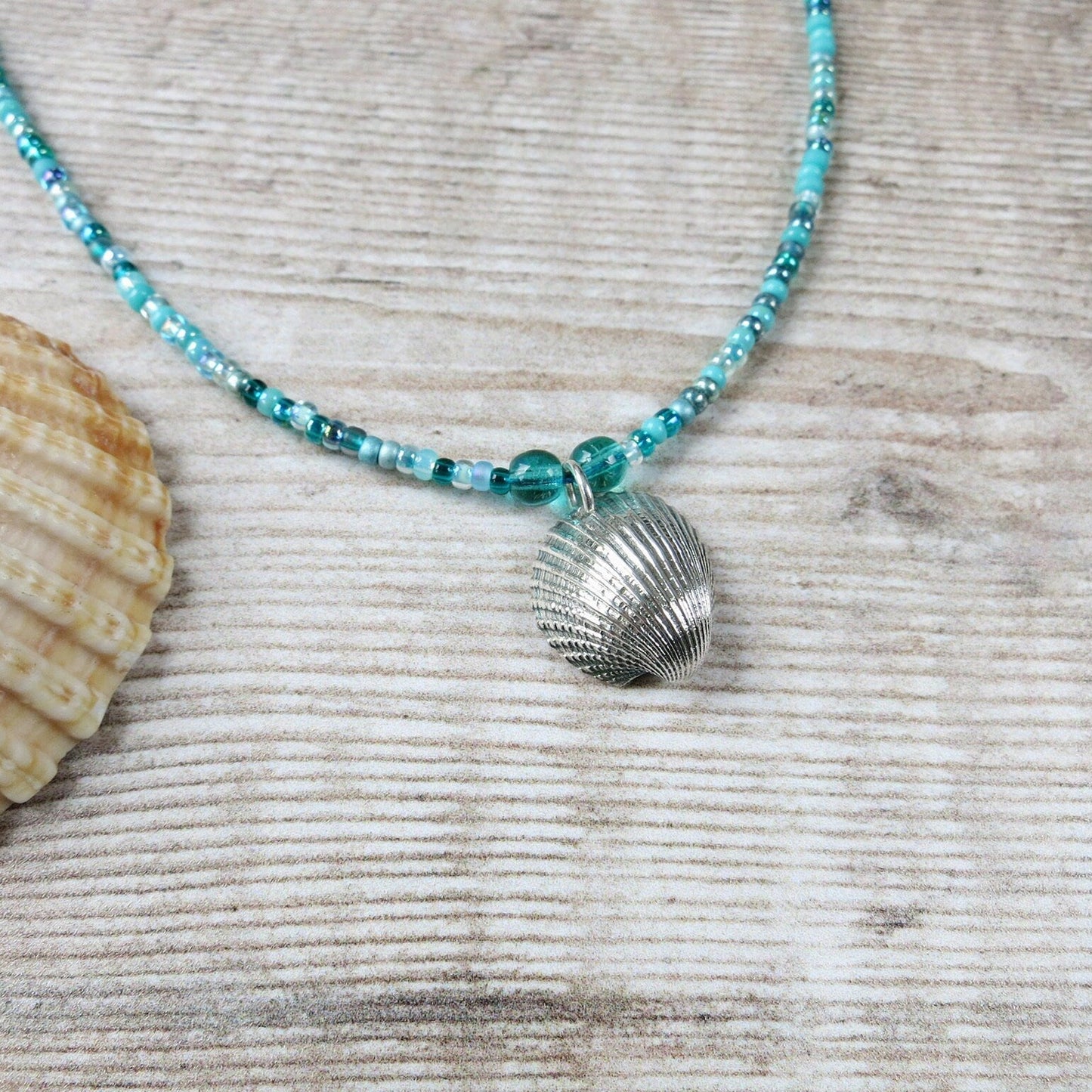Turquoise seed bead necklace with silver coated shell pendant laid on a textured surface
