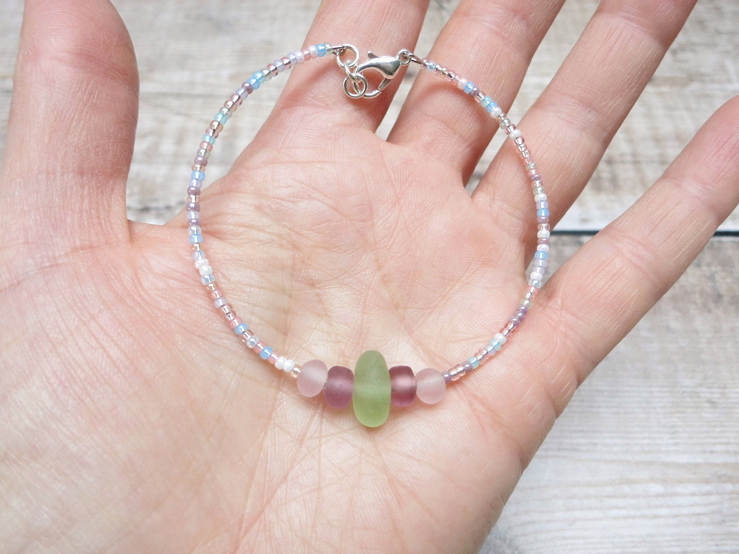 Pastel seed beaded bracelet with pale green sea glass held in a hand against a textured background