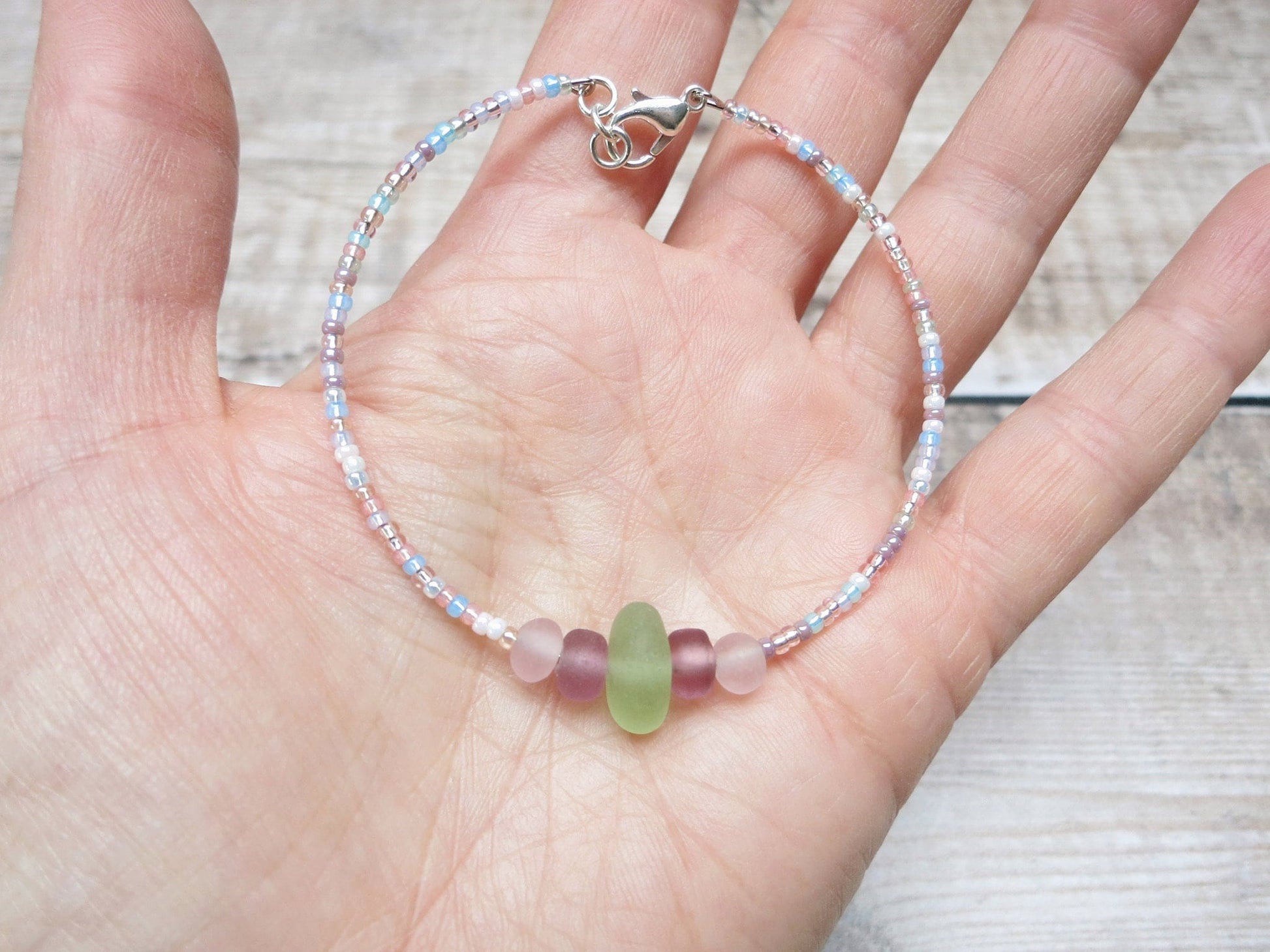 Pastel seed beaded bracelet with pale green sea glass held in a hand against a textured background