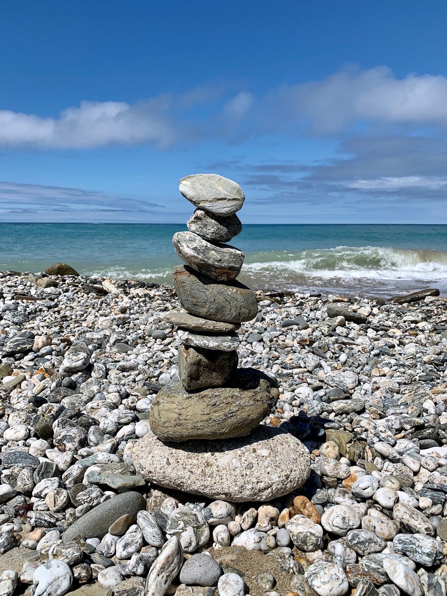 Stack of stones on a pebbly beach with ocean and sky in the background, the inspiration for the sea glass stack necklace