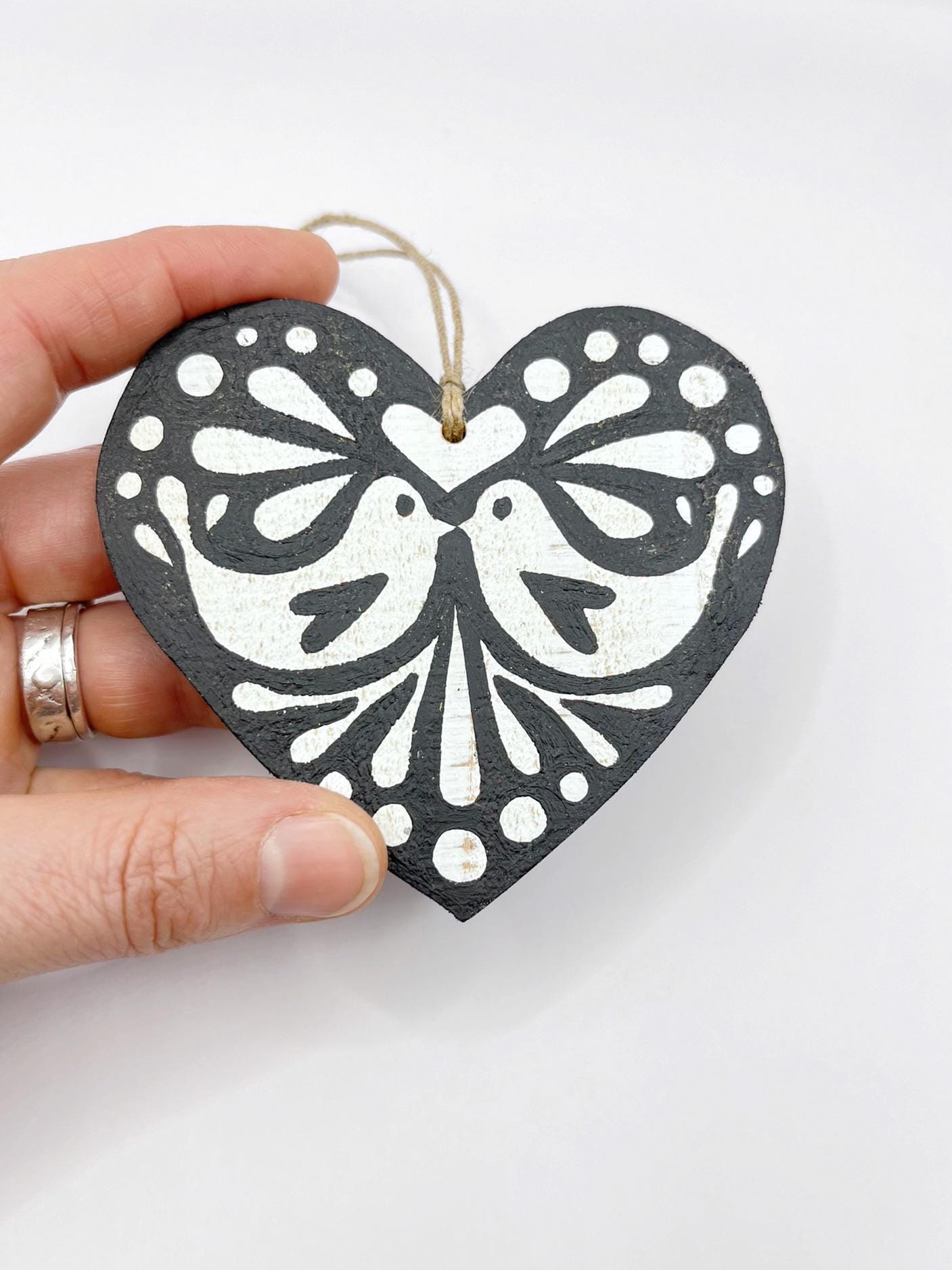 Black heart-shaped wooden hanging decoration with folk style love bird print   held in a hand against a white background
