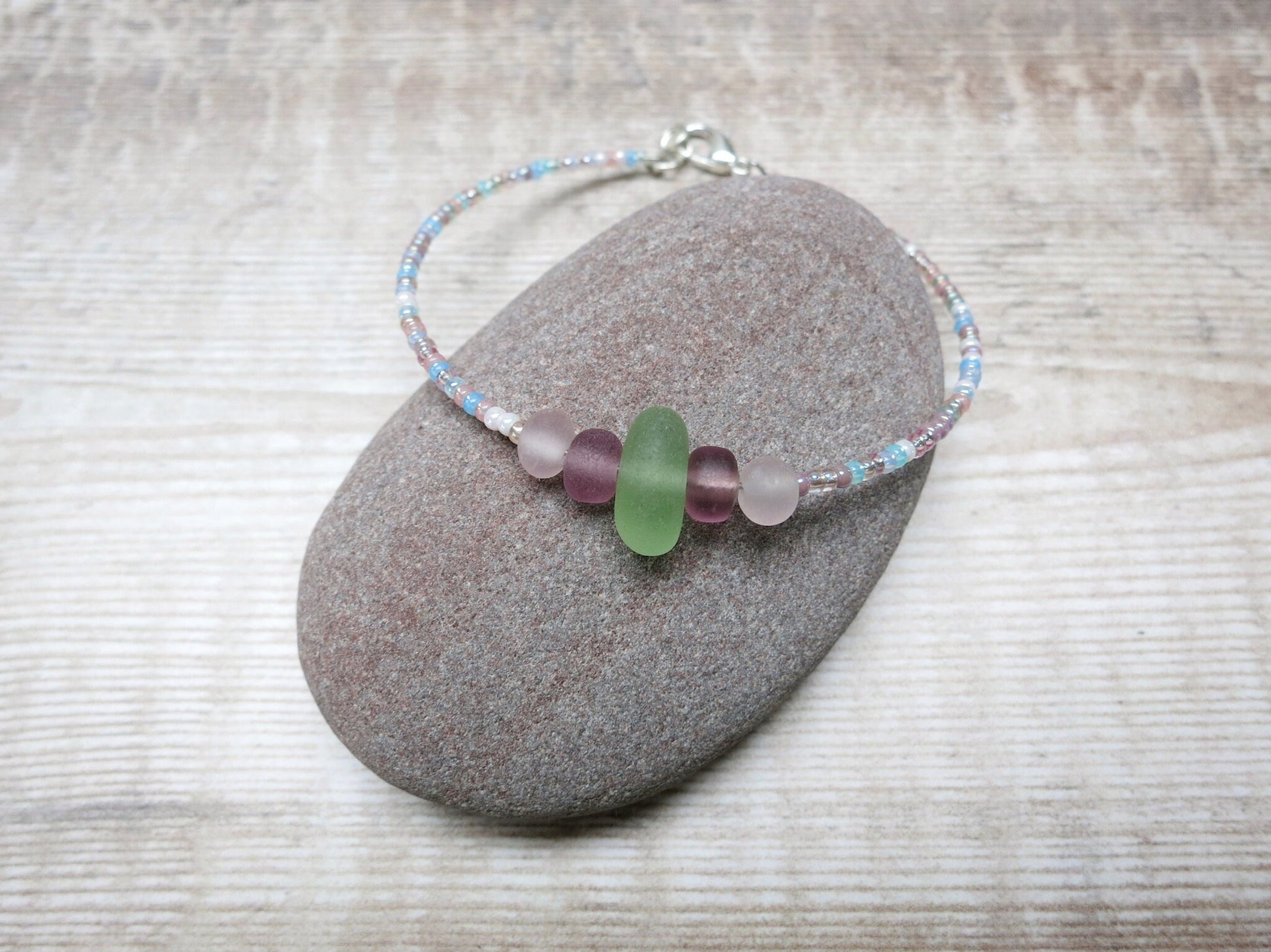 Pastel seed beaded bracelet with pale green sea glass laid on a pebble