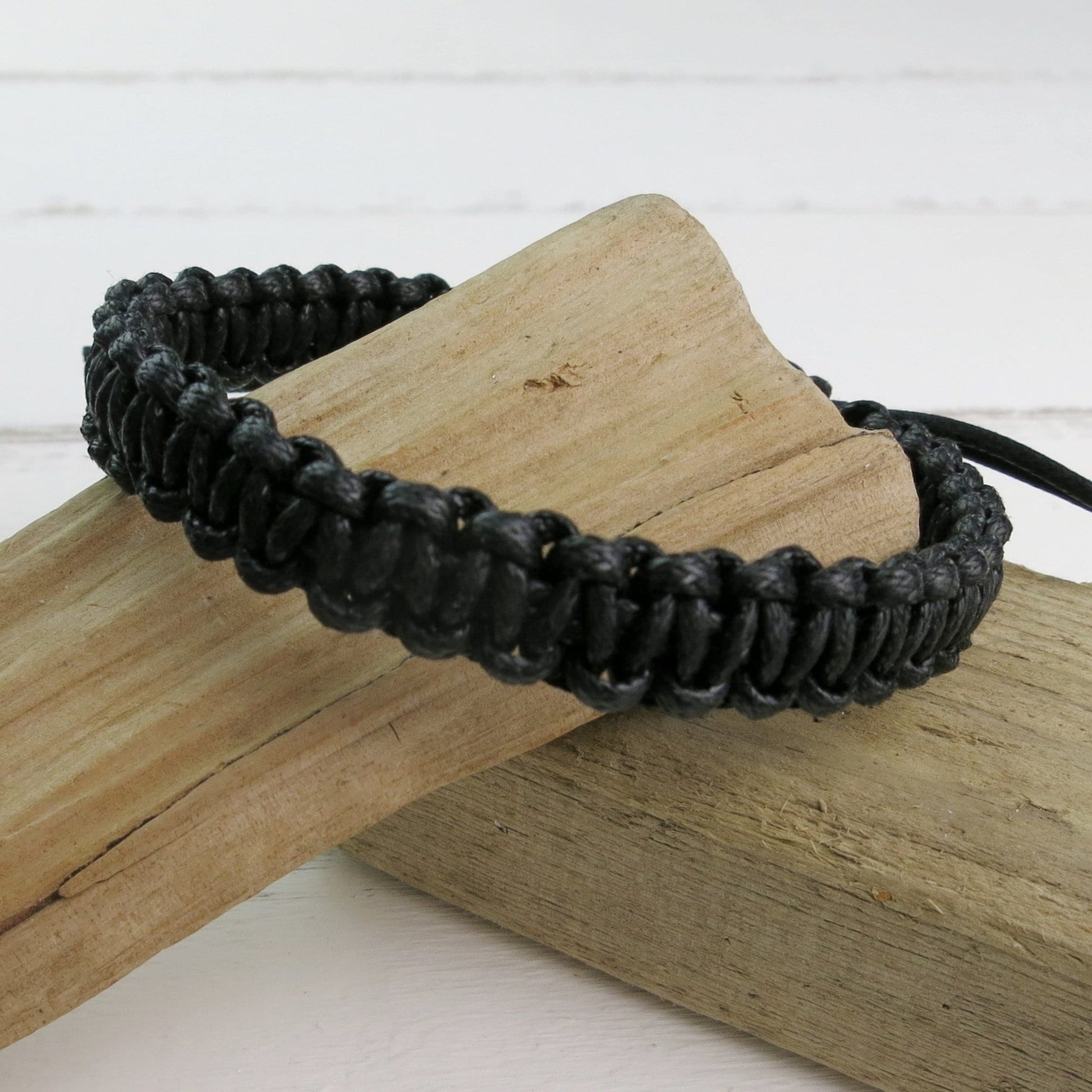 Black macrame bracelet laid on driftwood with a white background