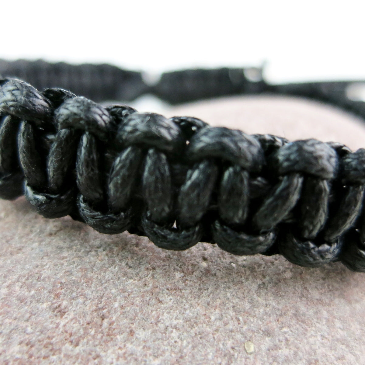 Close-up of a black braided bracelet on a textured surface