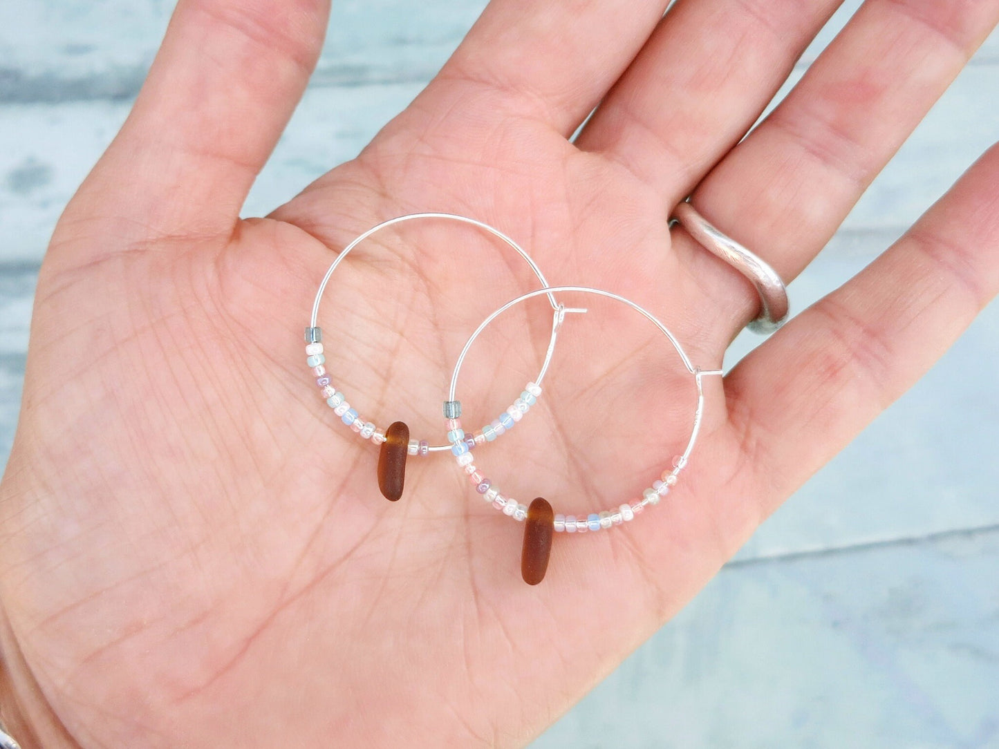 Pair of larger beaded hoop earrings held in a hand against a light blue background