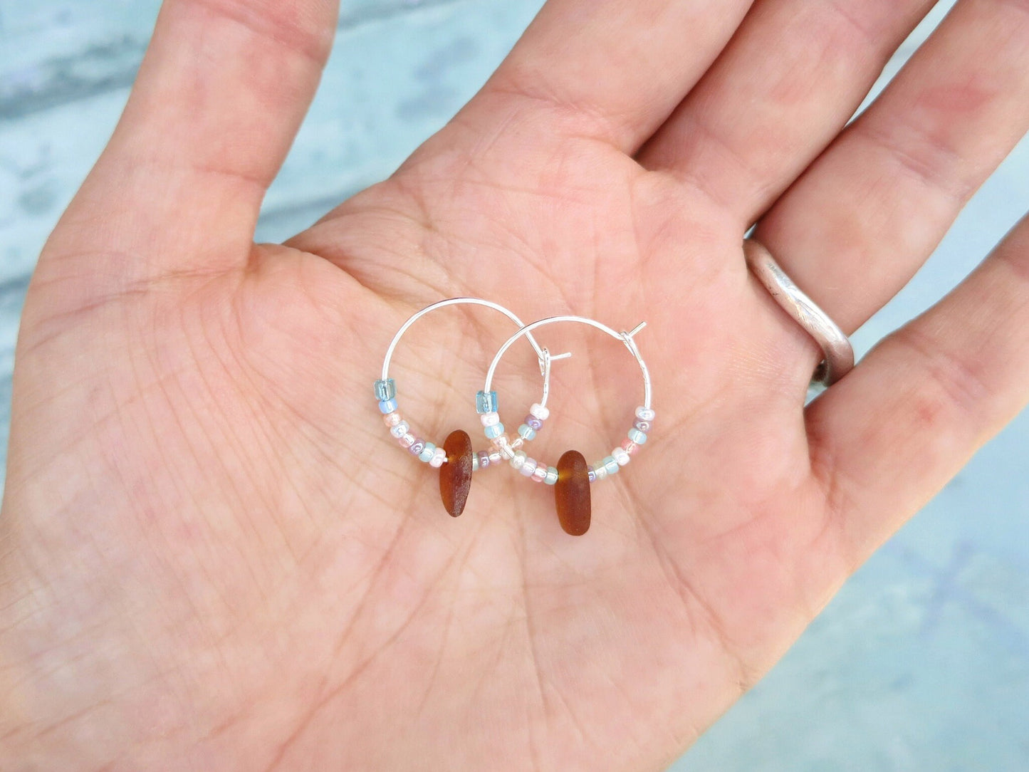 Pair of small beaded hoop earrings held in a hand against a pale blue background
