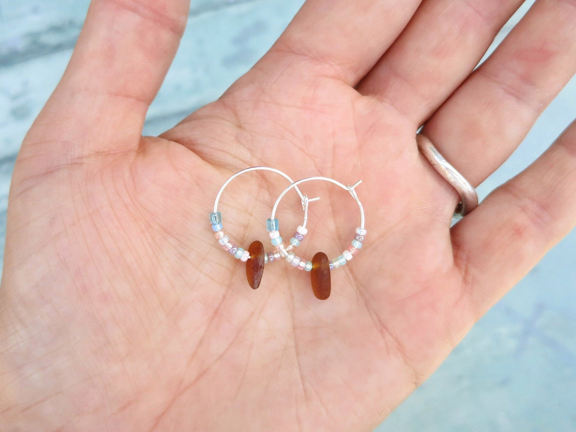 Pair of small beaded hoop earrings held in a hand against a pale blue background