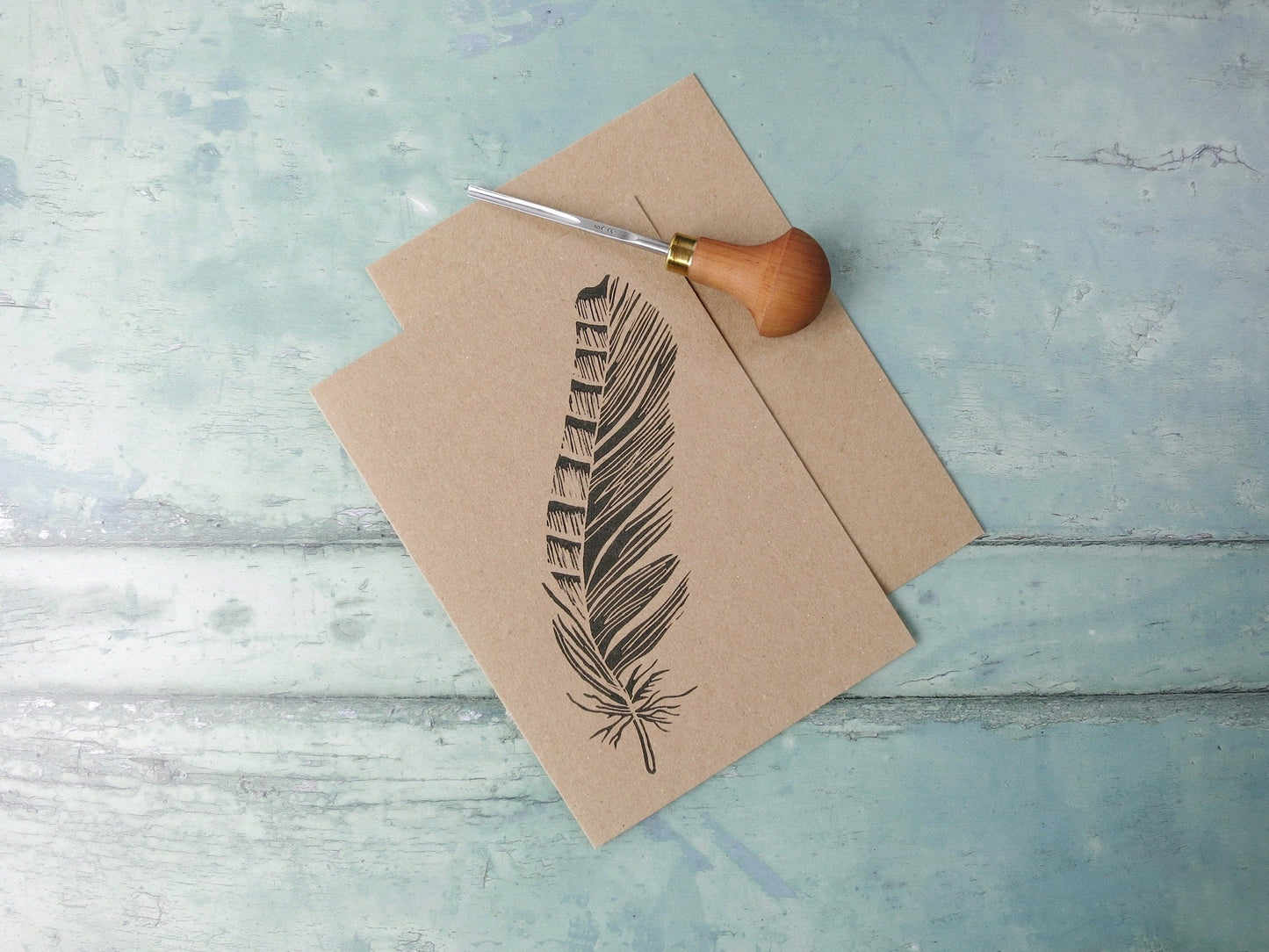 Kraft paper card with an original feather lino print laid on a wooden surface