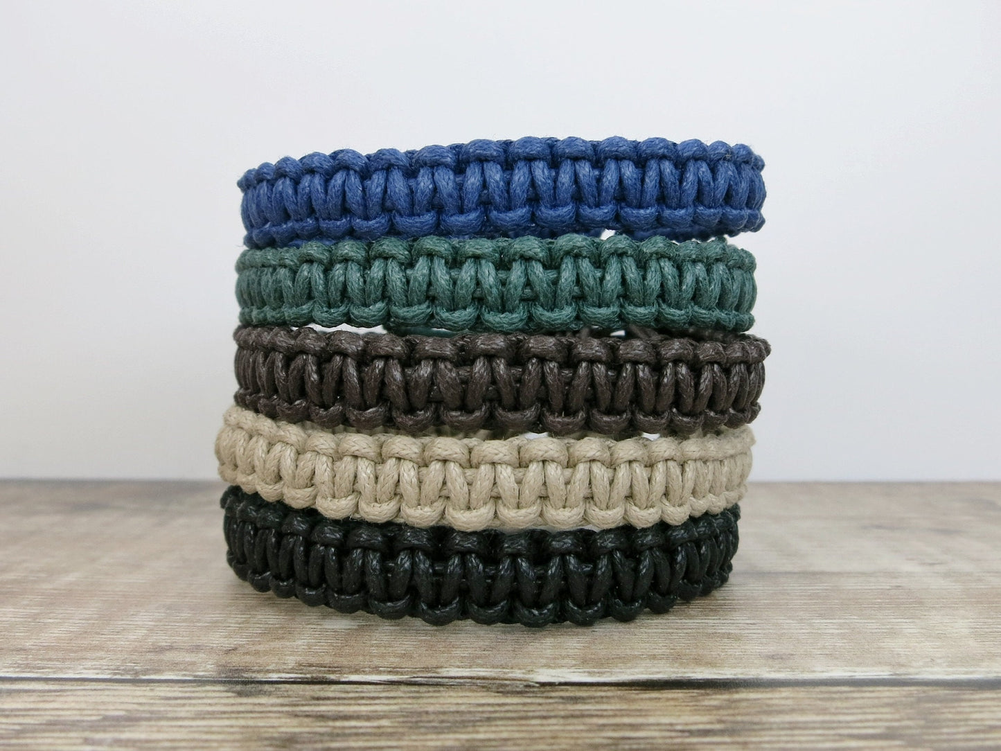 Stack of five macrame bracelets in various colours on a wooden surface.