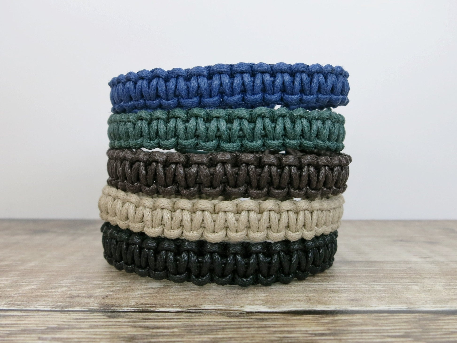Stack of five macrame bracelets in various colours on a wooden surface.