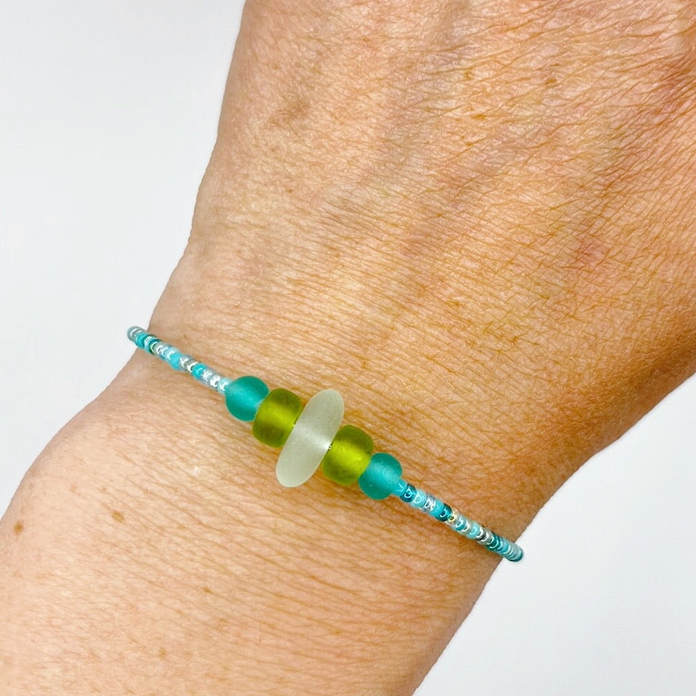 A close-up of a person's wrist wearing the turquoise beaded bracelet with lime and sea green frosted glass beads and a piece of sea foam coloured Cornish sea glass.