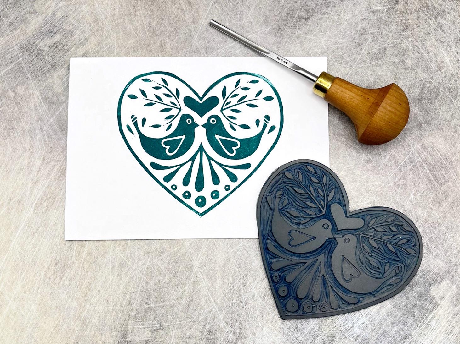 White card with original lino printed green heart design featuring two love birds. Photo includes lino and cutting tool.