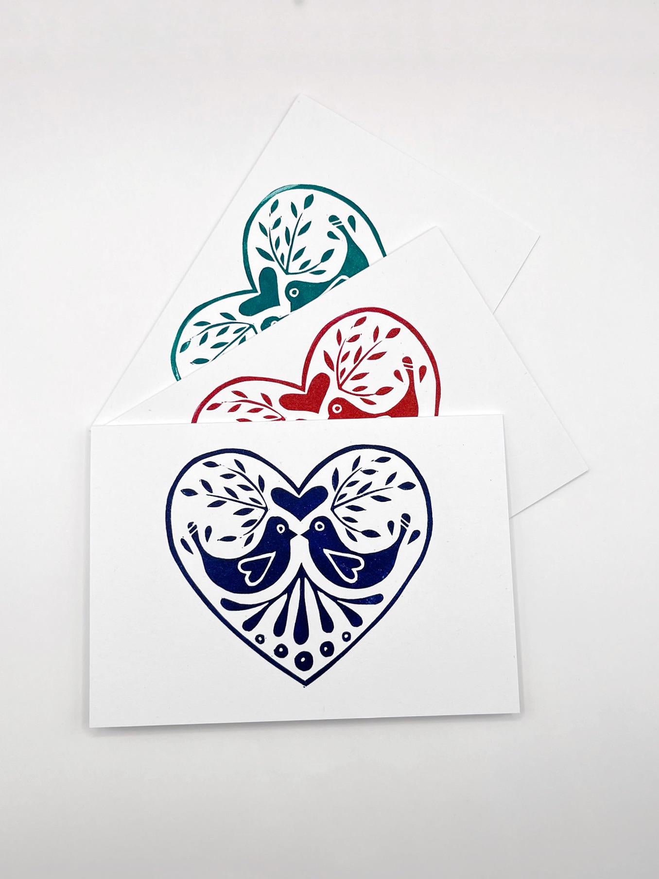 Set of three original lino printed heart design cards in red, blue and green, laid on a white background.