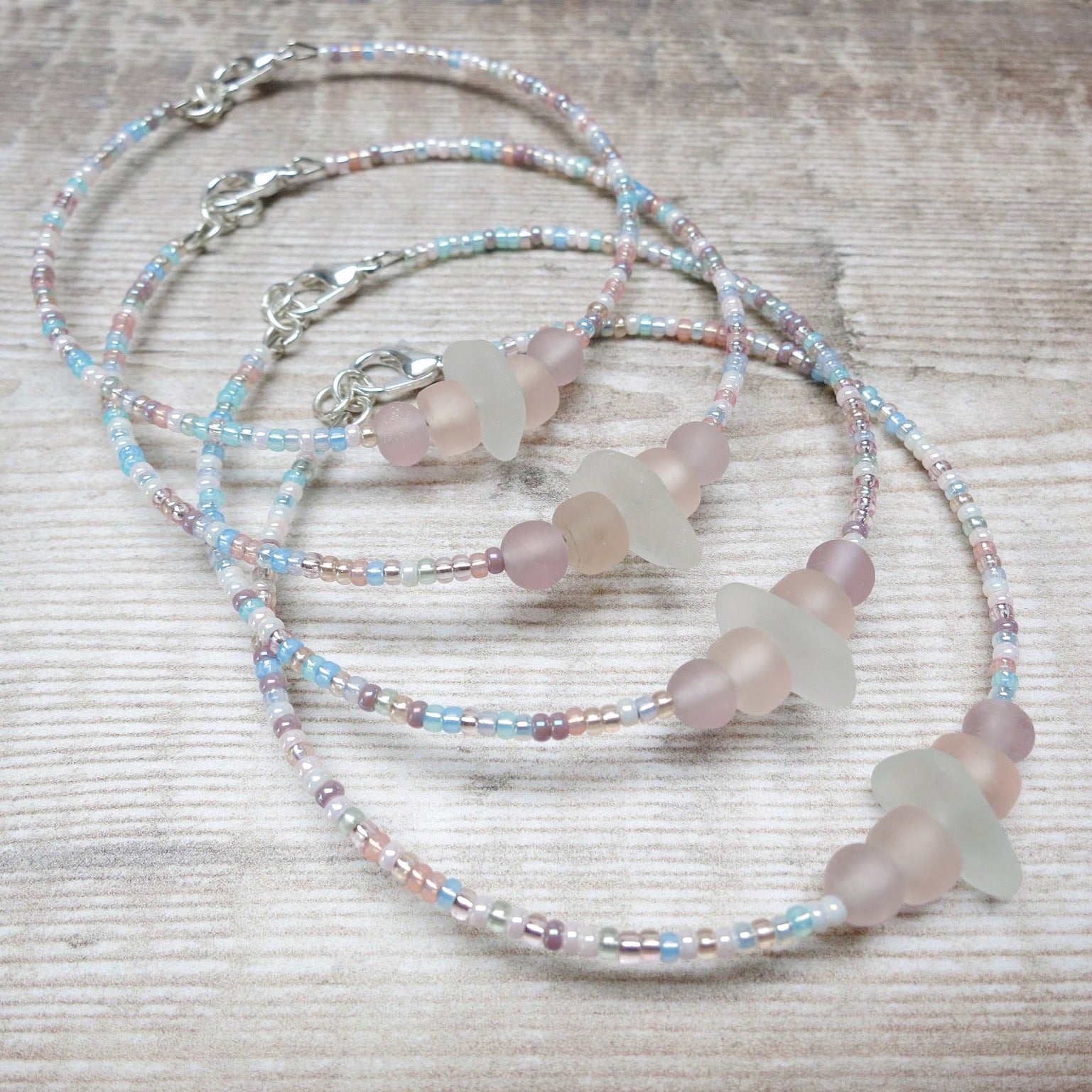 Four bracelets with white sea glass and pastel beads laid against a wooden background