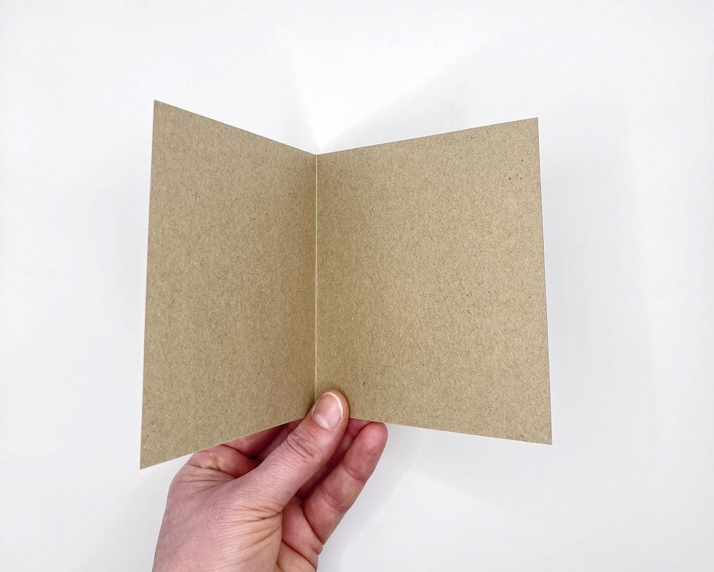 Hand holding a Kraft card open to show it is blank inside against a white background