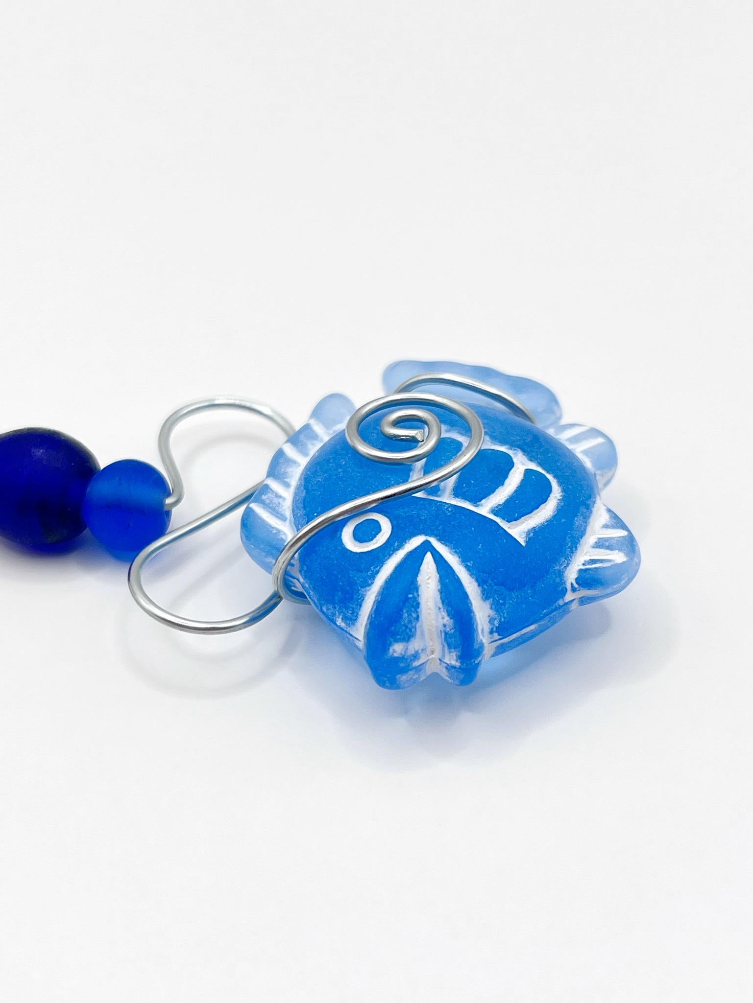 Close up of decorative hanging ornament with blue fish design, wire and glass beads on a white background