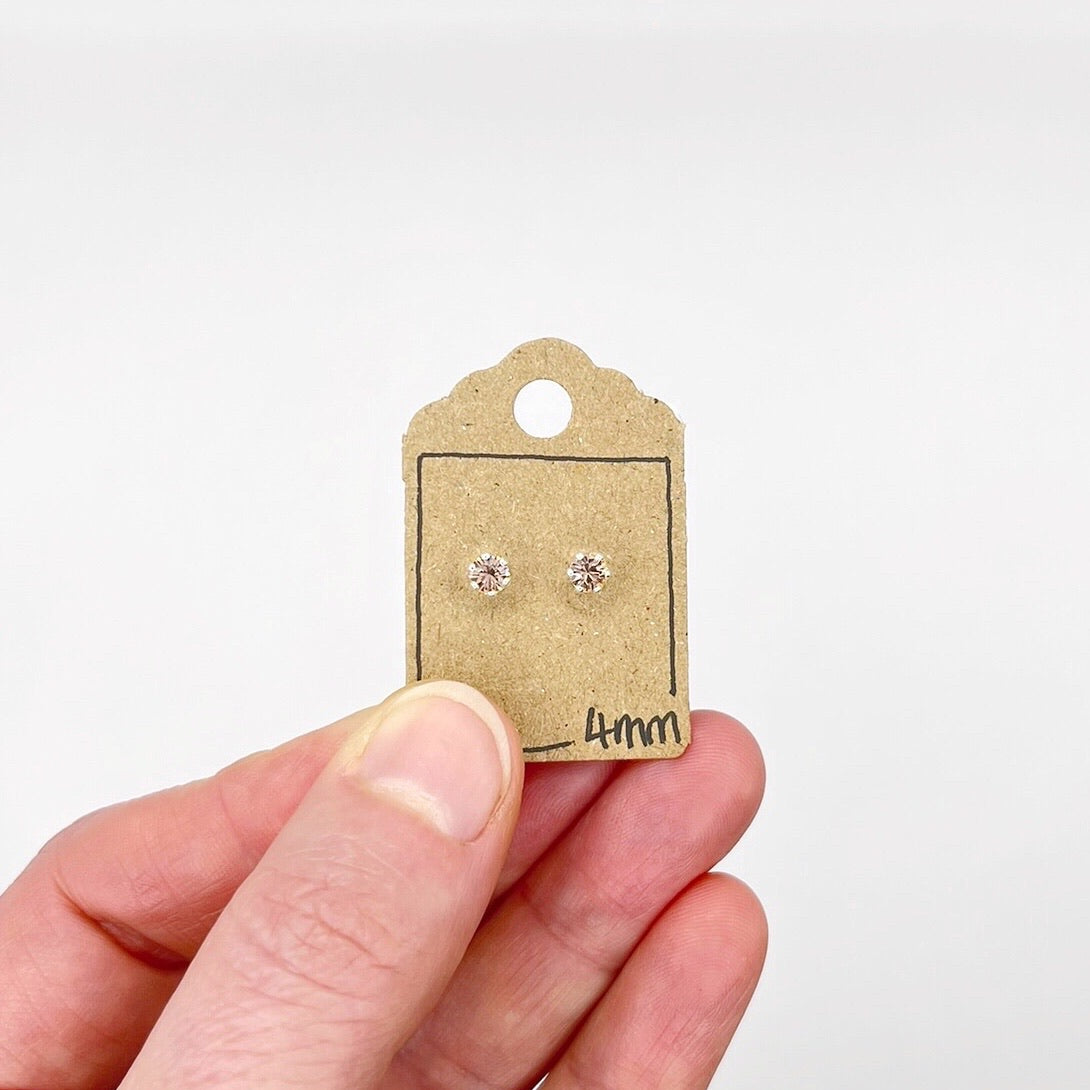Pair of silver stud earrings with cut glass on a cardboard backing held by a hand against a white background
