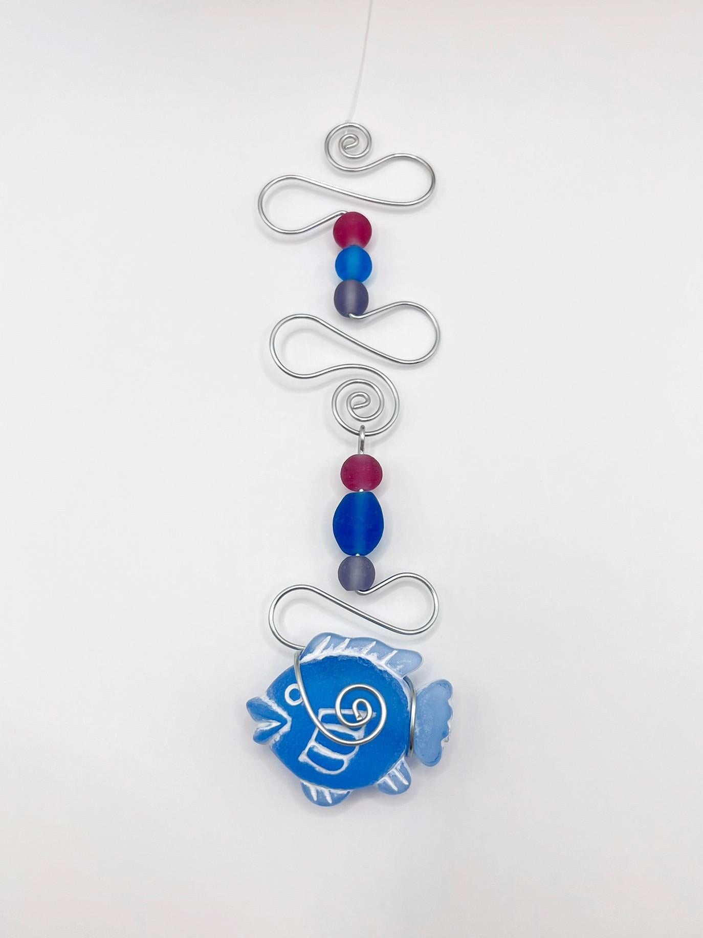 Decorative hanging ornament with blue fish design, wire and colourful beads, laid  on a white background