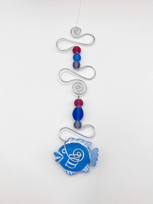 Decorative hanging ornament with blue fish design, wire and colourful beads, laid  on a white background