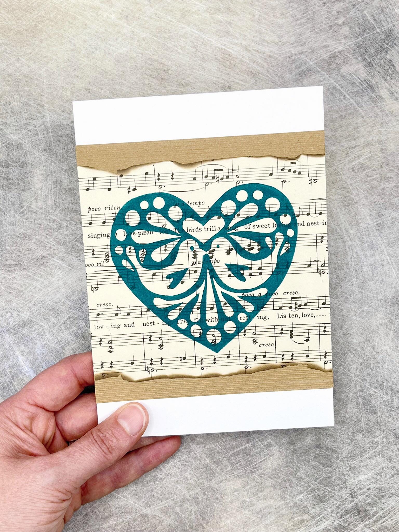 Card with decorative heart design on sheet music background held by a hand.
