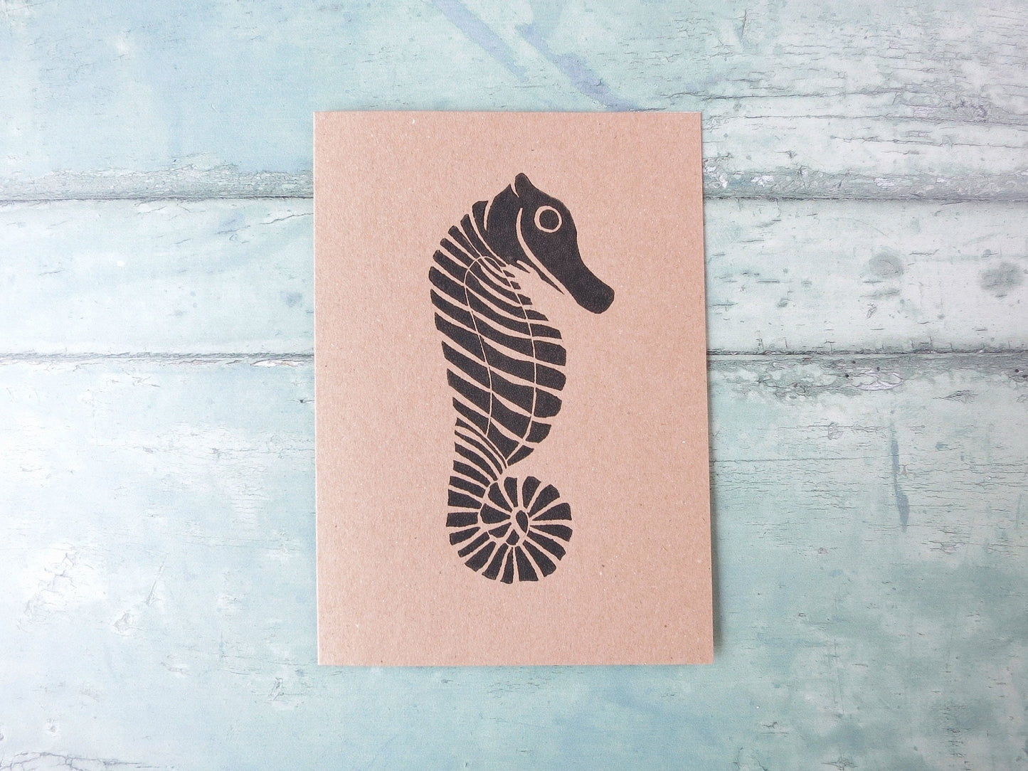 Kraft paper card with an original seahorse lino print laid on a textured blue surface. 