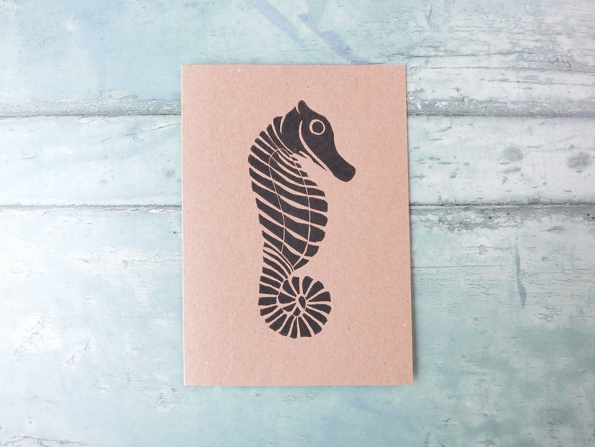 Kraft paper card with an original seahorse lino print laid on a textured blue surface. 