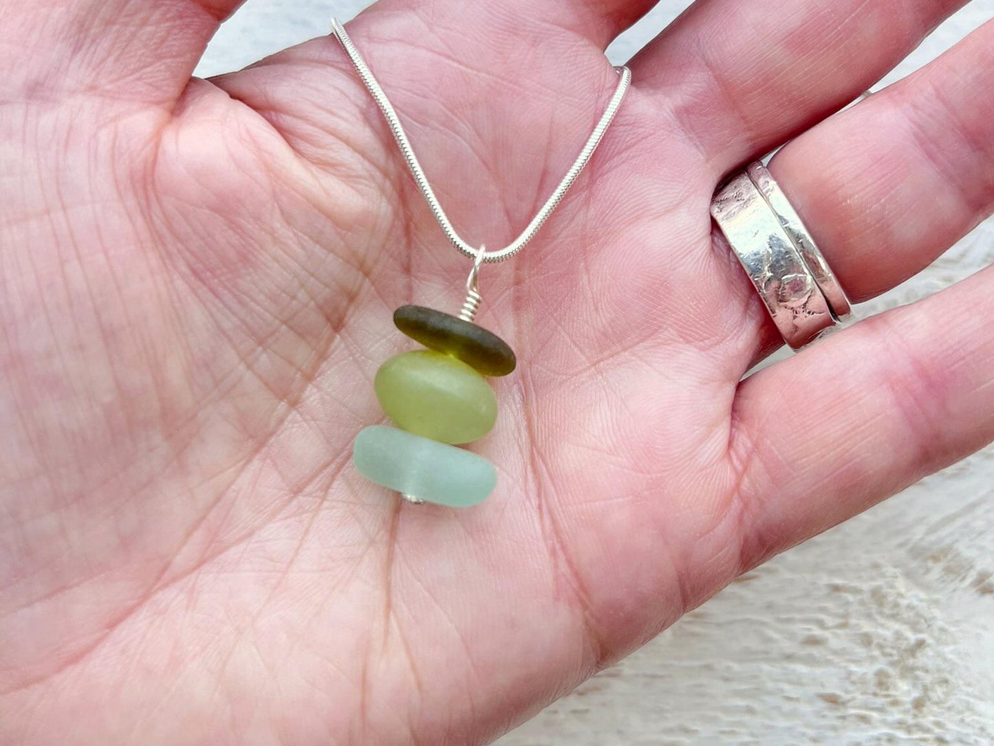 Necklace with green sea glass and a Jade bead held in a hand against a textured surface.